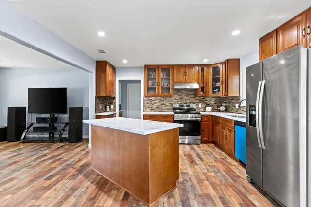 a kitchen with stainless steel appliances granite countertop a refrigerator a stove and a sink with wooden cabinets