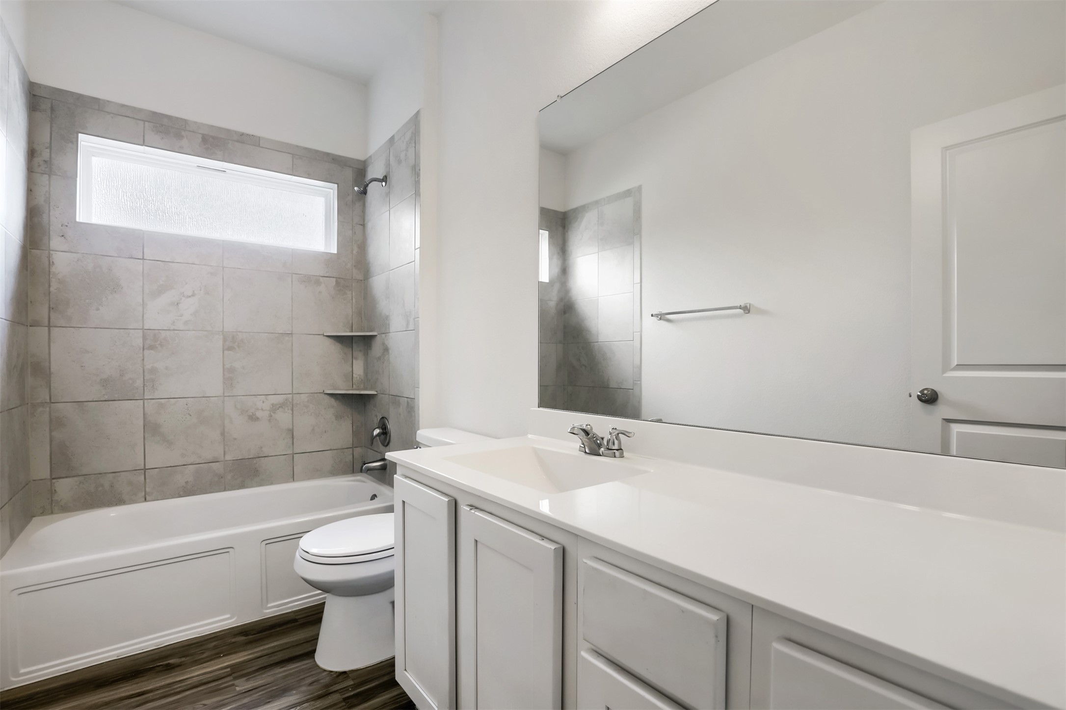 721 Mallow Road Leander, TX 78641 - Photo 18 of 22 Bathroom featuring a white vanity with a rectangular sink, a large mirror, a white bathtub with a tiled surround, and wood-look flooring