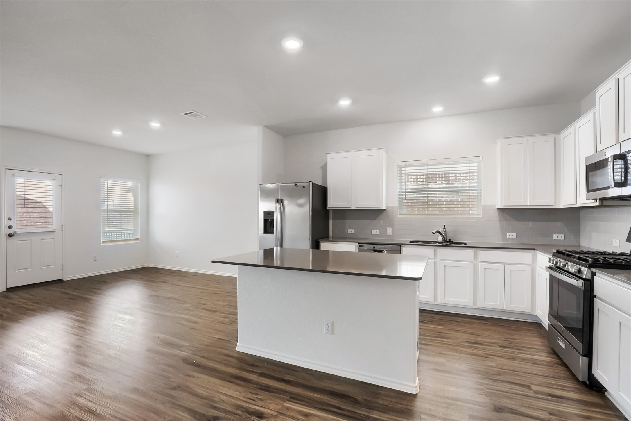 721 Mallow Road Leander, TX 78641 - Photo 7 of 22 Open concept kitchen and living area featuring dark wood-style flooring, white cabinetry, a kitchen island, and stainless steel appliances