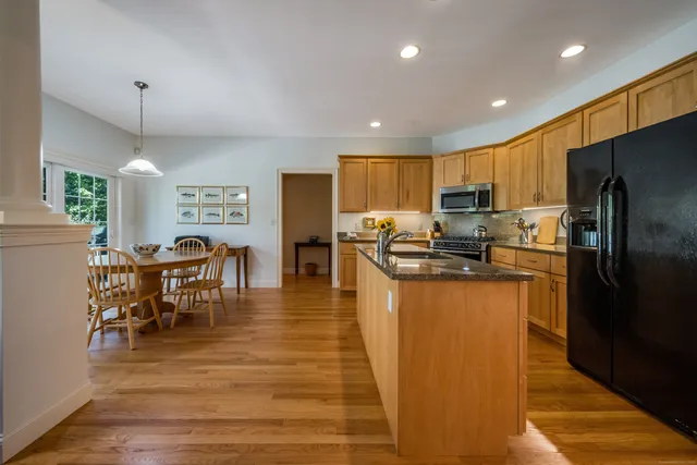 a kitchen with stainless steel appliances granite countertop a refrigerator a stove a sink a dining table and chairs with wooden floor