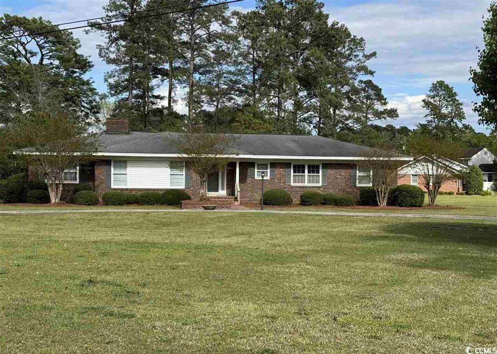 Single story home with a front lawn, a chimney, covered porch, and brick siding