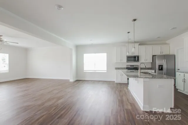 a kitchen with stainless steel appliances a microwave a stove a sink dishwasher a refrigerator and white cabinets with wooden floor