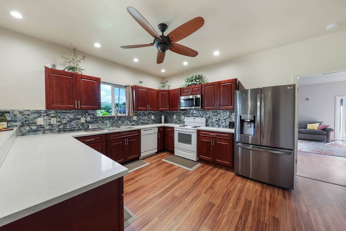 4598 Pueo Road, Unit B Kekaha, HI 96752 - Photo 7 of 27 a kitchen with stainless steel appliances granite countertop a refrigerator a sink dishwasher a stove with wooden floors and a dining table
