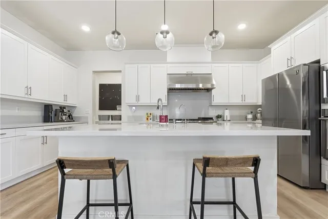 a kitchen with stainless steel appliances granite countertop a sink a stove a refrigerator and white cabinets with wooden floor