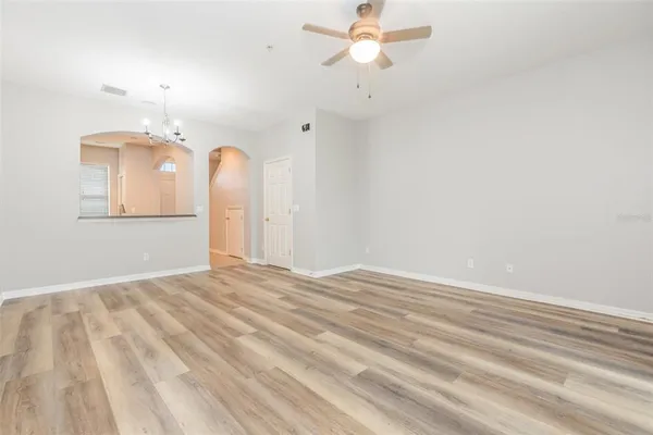 an empty room with a chandelier fan and wooden floor