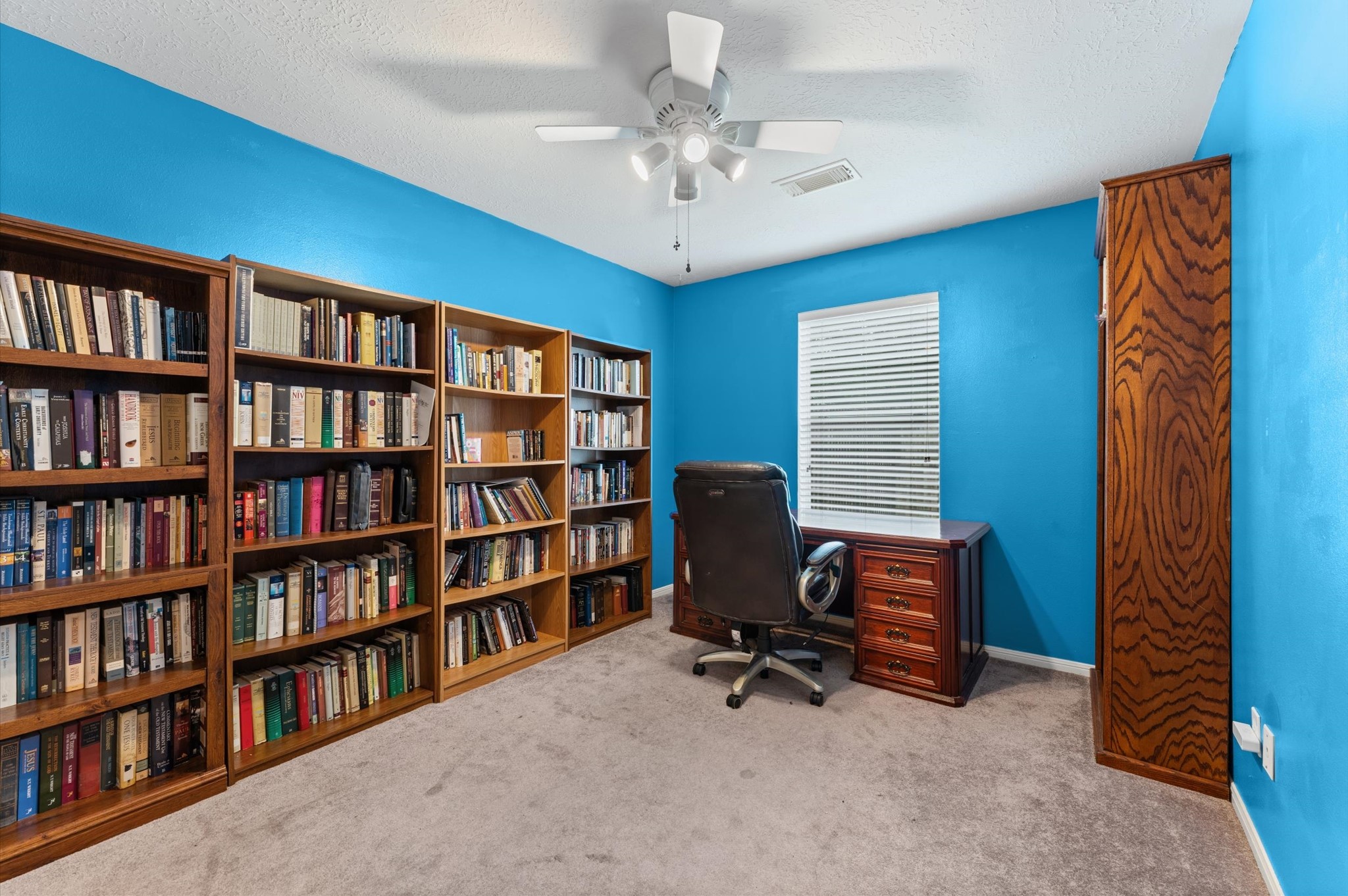 17618 Mill Springs Drive Spring, TX 77379 - Photo 18 of 26 This cozy study room features vibrant blue walls, built-in bookshelves filled with books, a comfortable office chair, and a wooden desk by the window, perfect for a home office or reading nook.