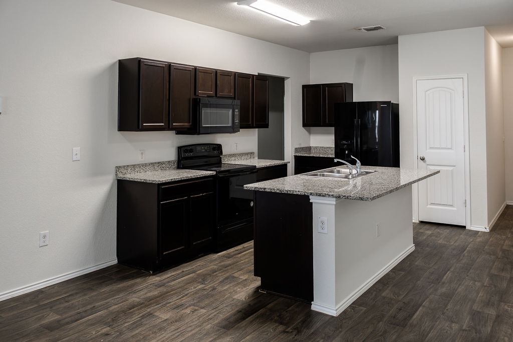 14915 Talus Road Manor, TX 78653 - Photo 7 of 20 Dark wood cabinetry and stone countertops accent this modern kitchen with a central island.