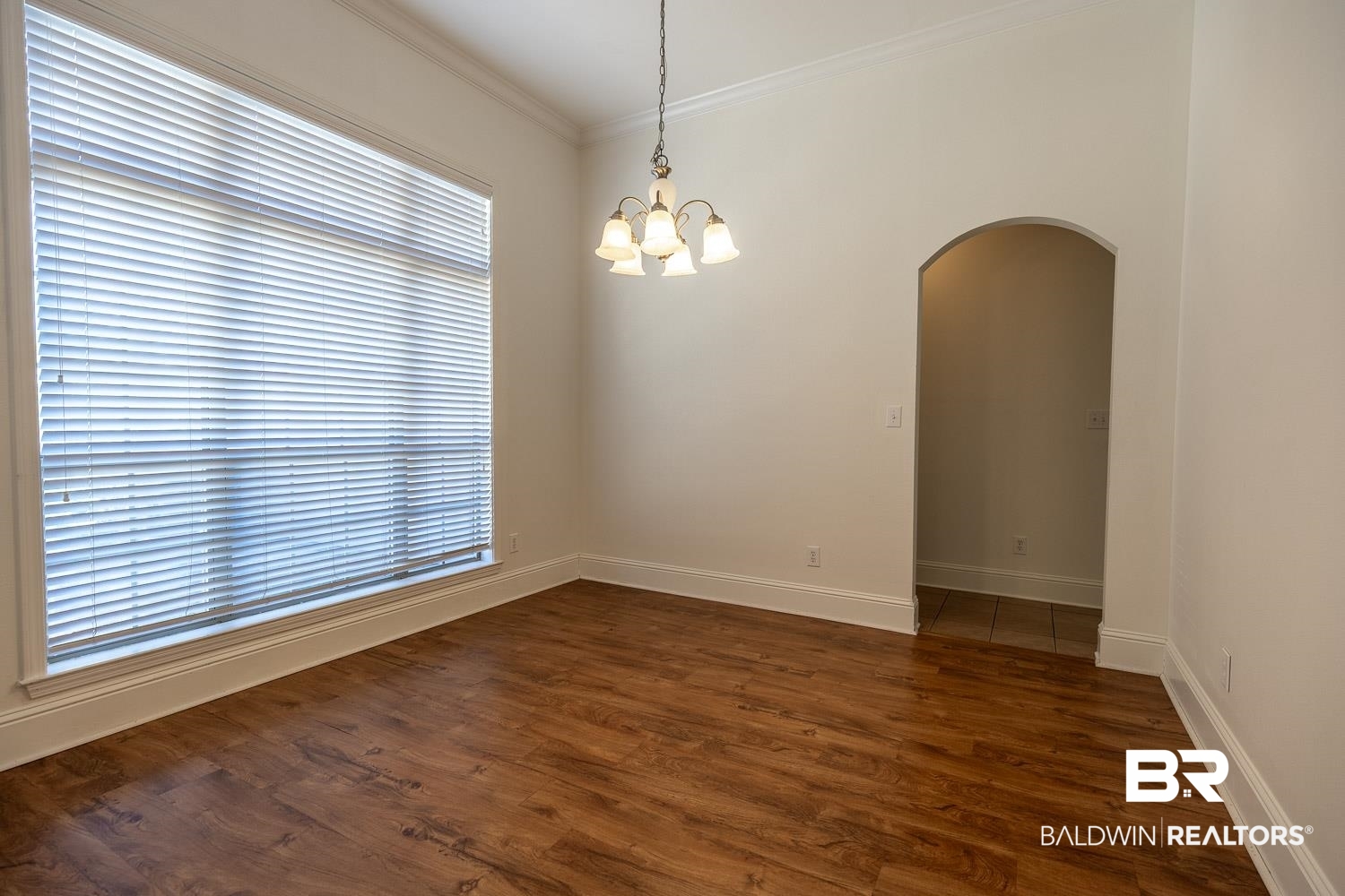 101 Normandy Street Fairhope, AL 36532 - Photo 2 of 18 Spare room featuring arched walkways, dark wood-style floors, crown molding, and a chandelier