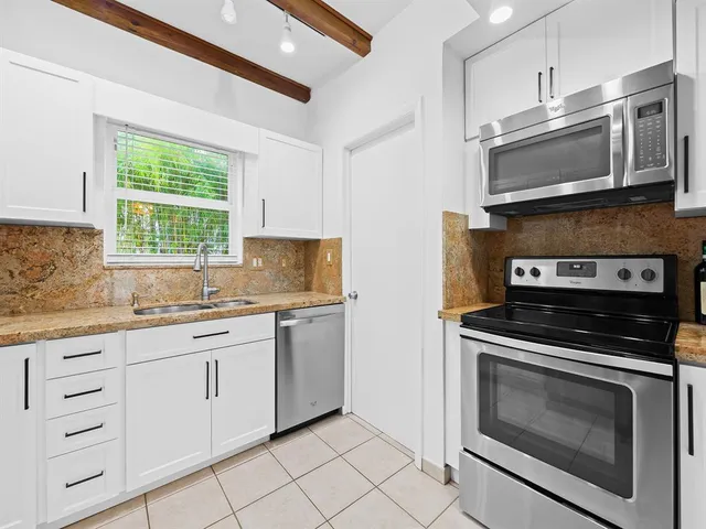a kitchen with granite countertop white cabinets stainless steel appliances and a window