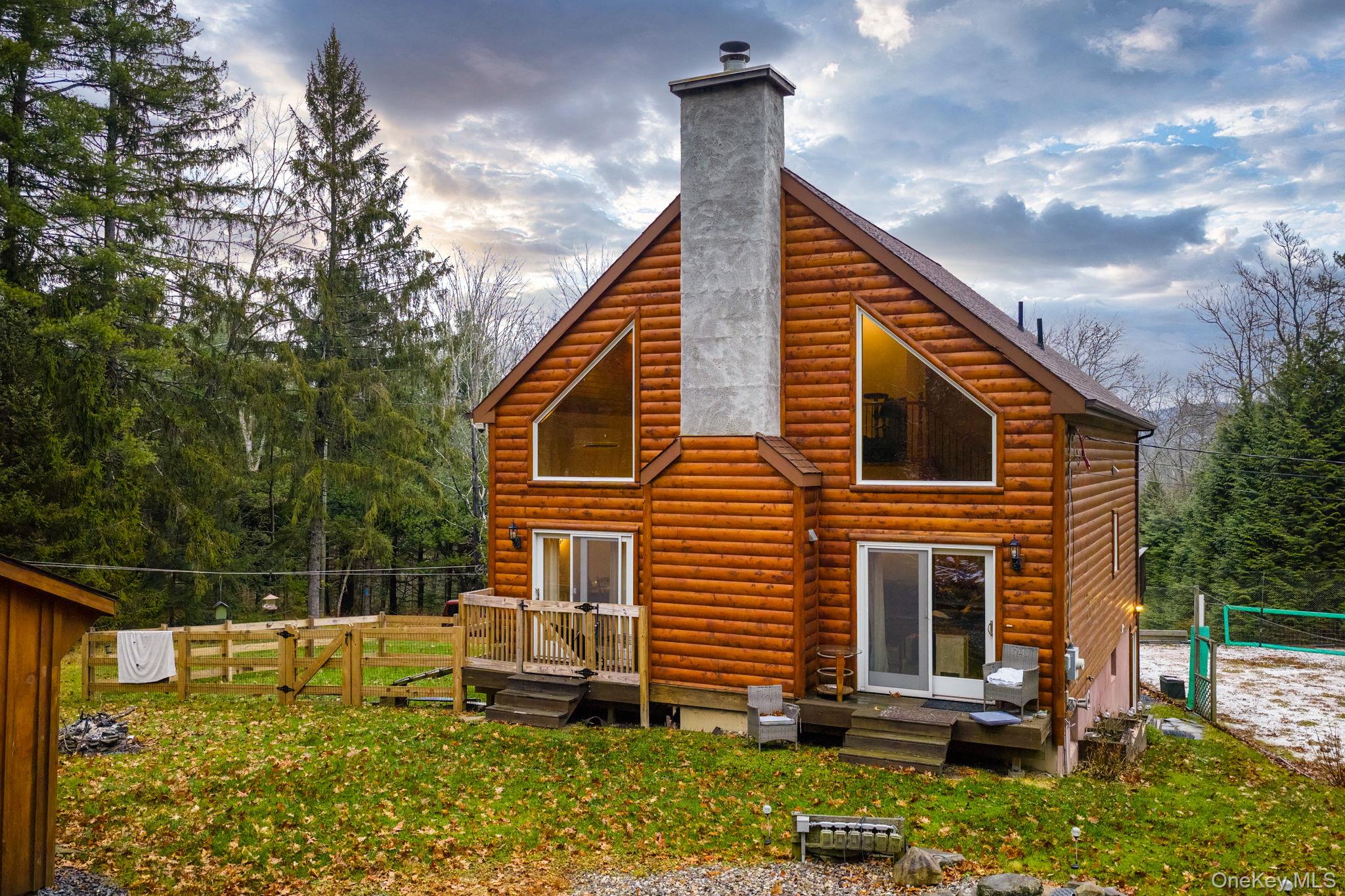 Back of house at dusk with faux log siding, a chimney, and a deck