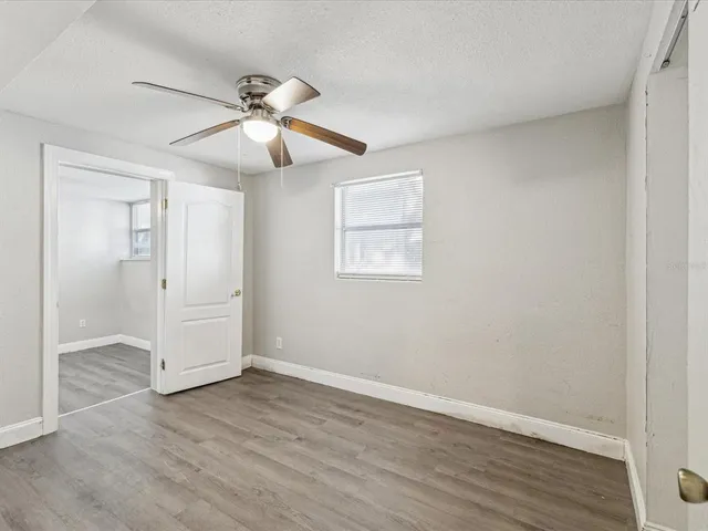an empty room with wooden floor ceiling fan and windows