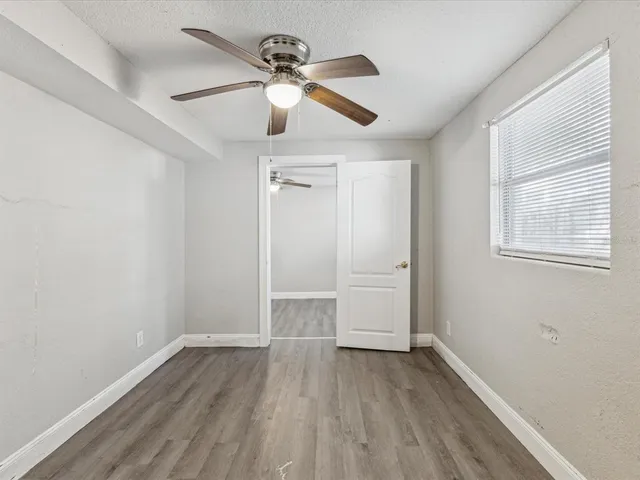 an empty room with wooden floor ceiling fan and windows