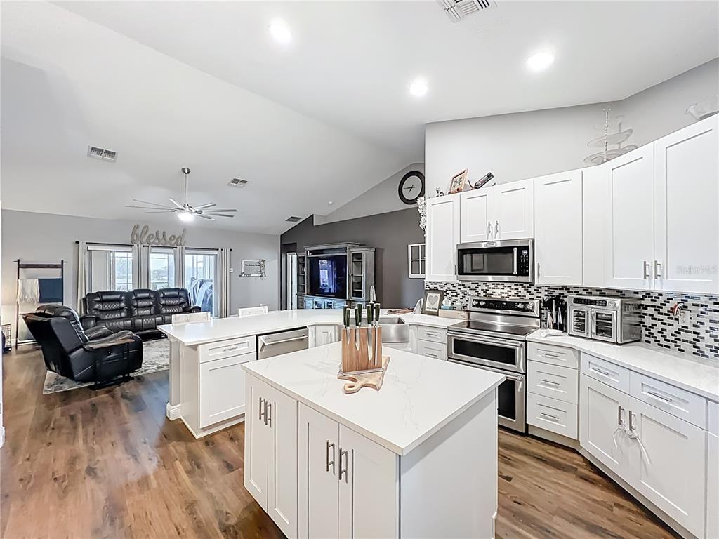 135 Blackstone Creek Road Groveland, FL 34736 - Photo 28 of 62 a kitchen with stainless steel appliances kitchen island granite countertop a stove top oven a sink a dining table and chairs with wooden floor