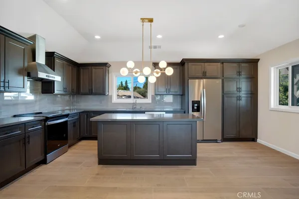 a kitchen with stainless steel appliances granite countertop a refrigerator a sink dishwasher a stove and a dining table with wooden floor