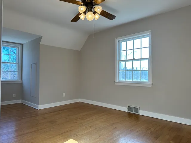 an empty room with wooden floor chandelier fan and windows
