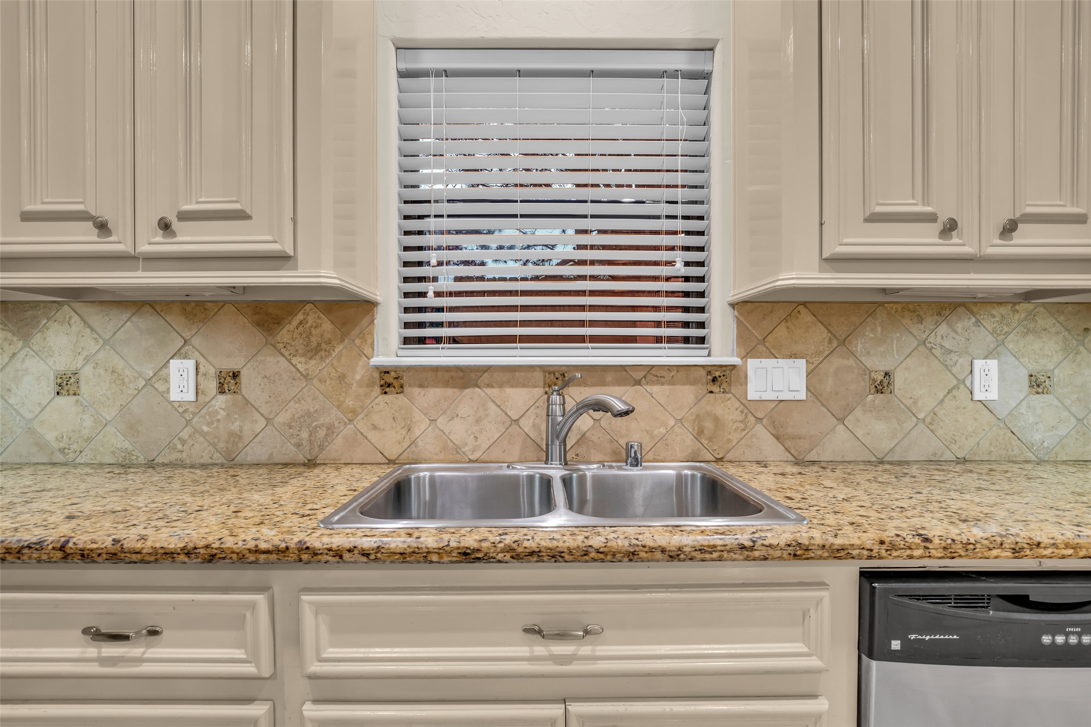 1898 Longmire Road, Unit 5 Conroe, TX 77304 - Photo 21 of 48 This kitchen features elegant cabinetry, a dual sink with a modern faucet, granite countertops, and a tile backsplash. Natural light filters through the window with blinds, creating a bright and inviting space.