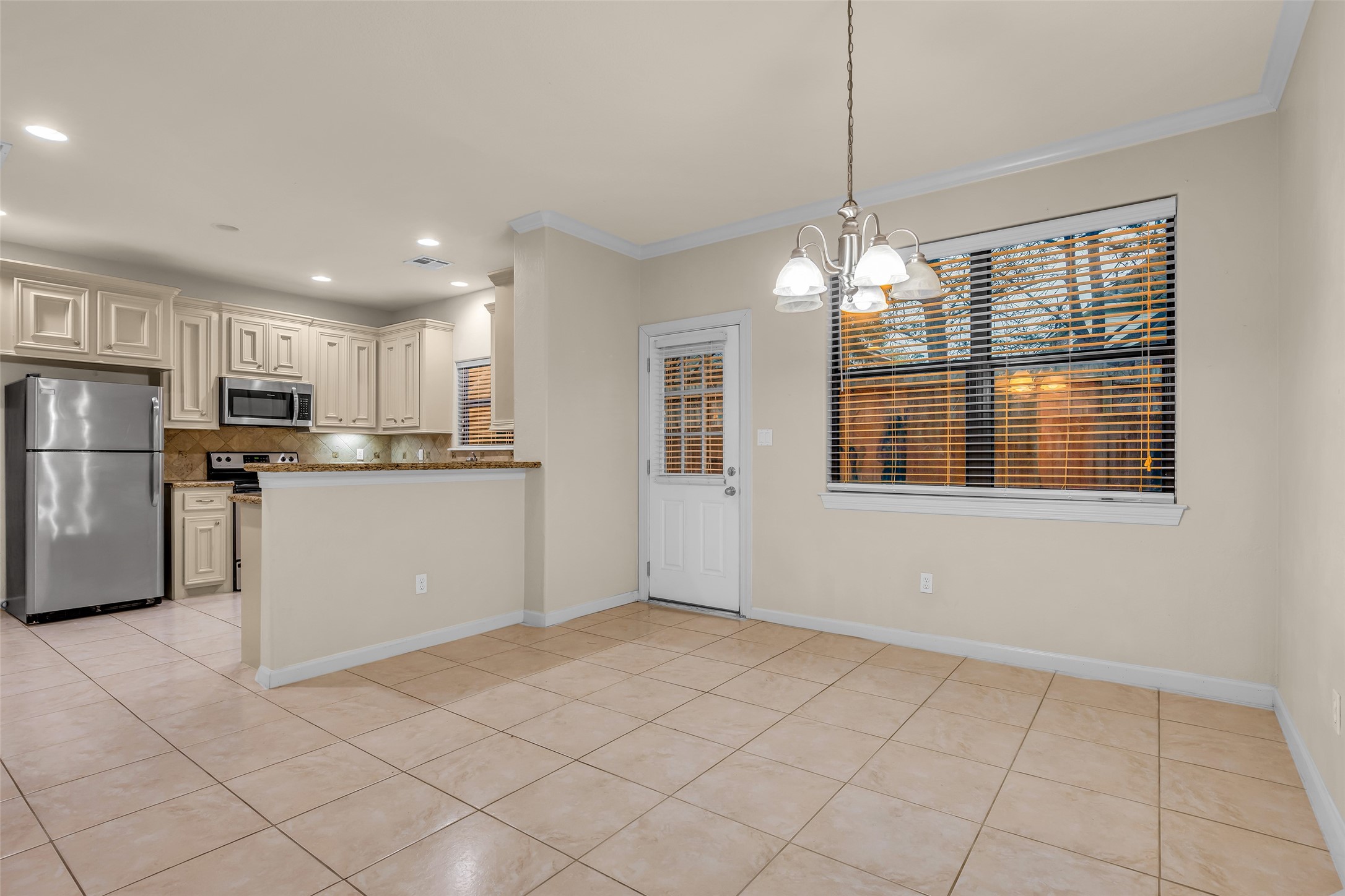 1898 Longmire Road, Unit 5 Conroe, TX 77304 - Photo 23 of 48 This photo showcases a bright, open-concept kitchen and dining area. It features modern stainless steel appliances, light cabinetry, and tile flooring. The space is well-lit with ample natural light from a large window and a stylish chandelier.