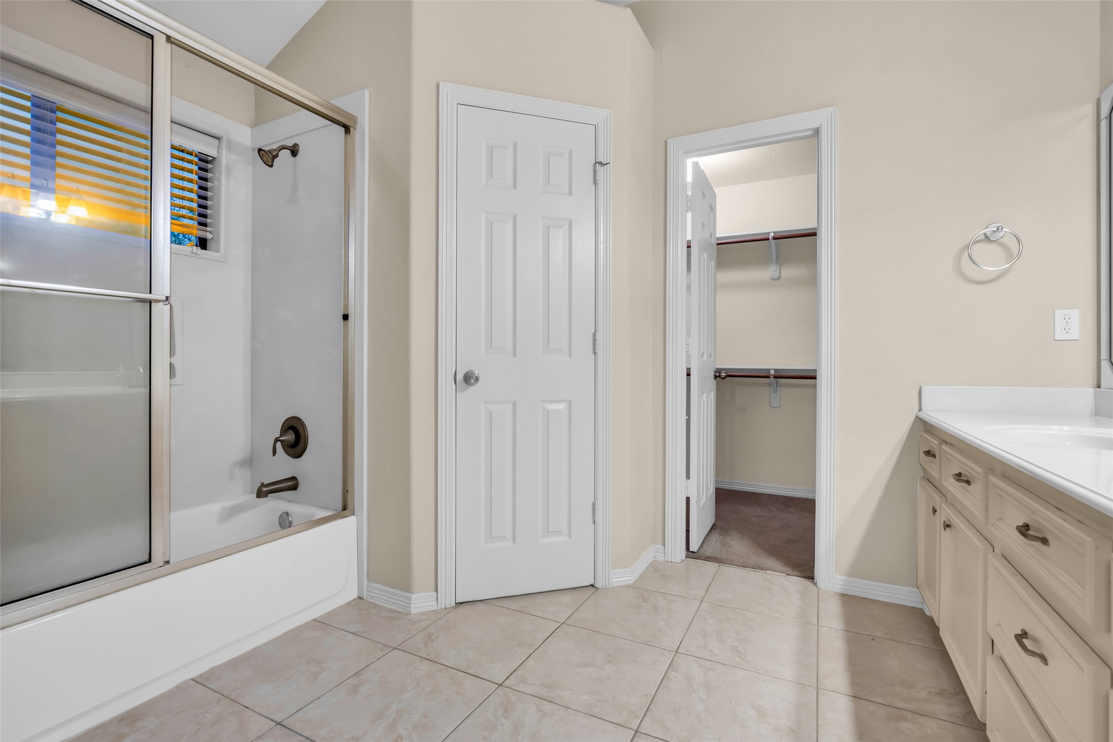 1898 Longmire Road, Unit 5 Conroe, TX 77304 - Photo 35 of 48 This bathroom features a bathtub with sliding glass doors, a double-sink vanity with ample storage, and access to a walk-in closet. The room has neutral tile flooring and soft beige walls, creating a warm, inviting atmosphere.
