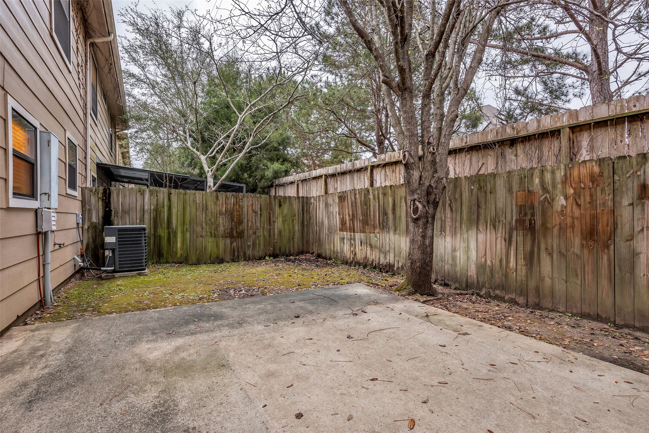 1898 Longmire Road, Unit 5 Conroe, TX 77304 - Photo 45 of 48 This photo shows a small, fenced backyard featuring a concrete patio area, a mature tree, and some grass. It provides a private outdoor space suitable for relaxation or small gatherings.