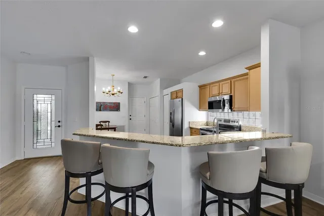 a kitchen with stainless steel appliances granite countertop a dining table chairs refrigerator and sink