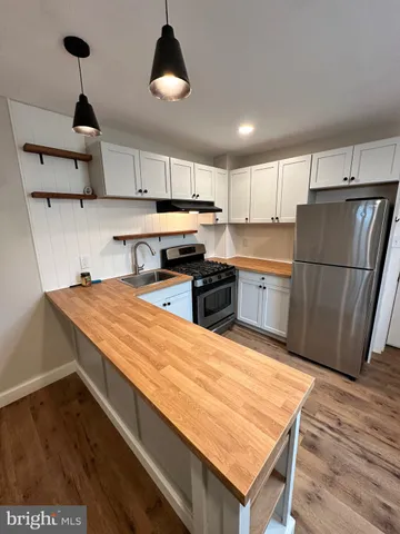 a kitchen with stainless steel appliances granite countertop a refrigerator a sink dishwasher a stove and white countertops with wooden floor