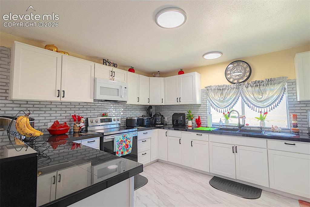 3425-3435 Wiesner Road Calhan, CO 80808 - Photo 19 of 25 Kitchen featuring white microwave, stainless steel electric range, a sink, dark countertops, and light marble finish floors