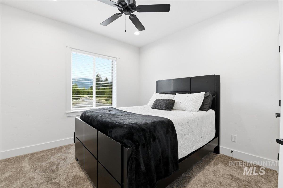 13152 Hawks Bay Road Donnelly, ID 83615 - Photo 22 of 29 Bright bedroom featuring a large window with mountain scenery, plush carpeting, a modern ceiling fan, and white walls