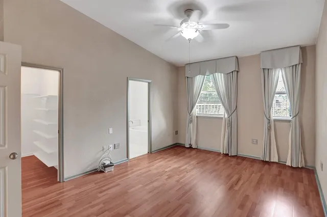 an empty room with wooden floor chandelier fan and windows