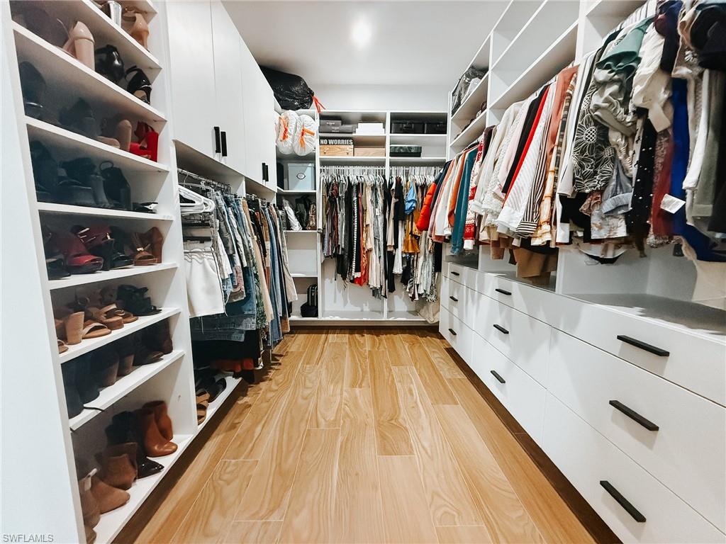 1702 Ludlow Road Marco Island, FL 34145 - Photo 27 of 47 Custom closet with wood-finish flooring, white built-in shelving, integrated drawers with dark hardware, and ample hanging storage