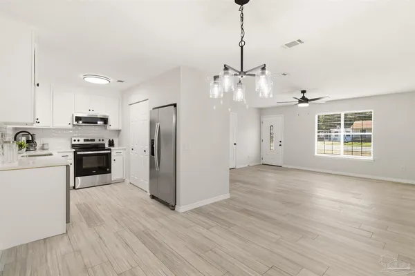 a kitchen with stainless steel appliances granite countertop a refrigerator a sink dishwasher a stove and white cabinets with wooden floor