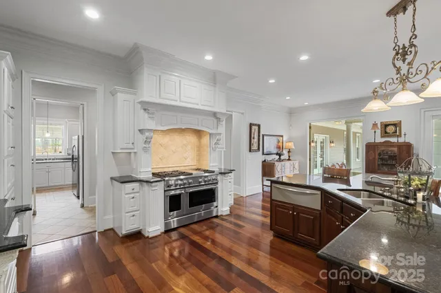 a kitchen with stainless steel appliances granite countertop a stove top oven a sink dishwasher and a refrigerator with wooden floor