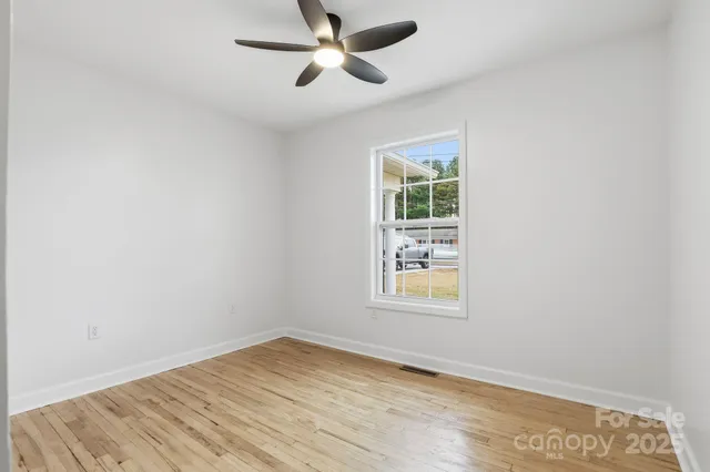 an empty room with wooden floor ceiling fan and windows