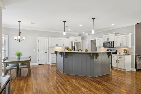 a dining room with wooden floor a chandelier a glass table and chairs