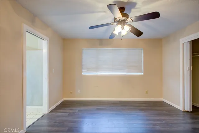 a view of an empty room with wooden floor and a ceiling fan
