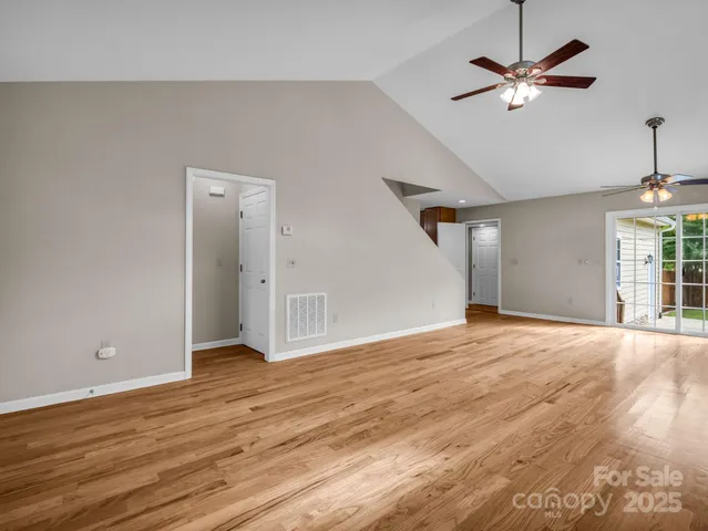 a view of an empty room with wooden floor and a ceiling fan