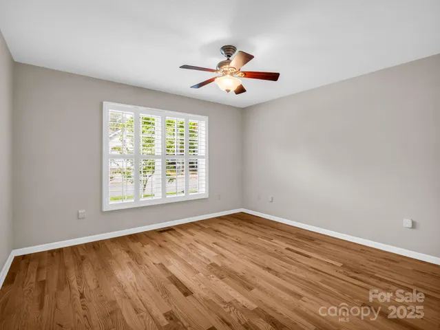 an empty room with wooden floor fan and windows