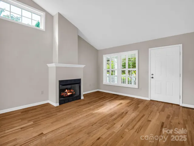 a view of an empty room with wooden floor fireplace and a window