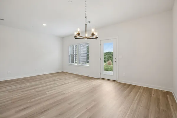a view of an empty room with wooden floor kitchen view and a window