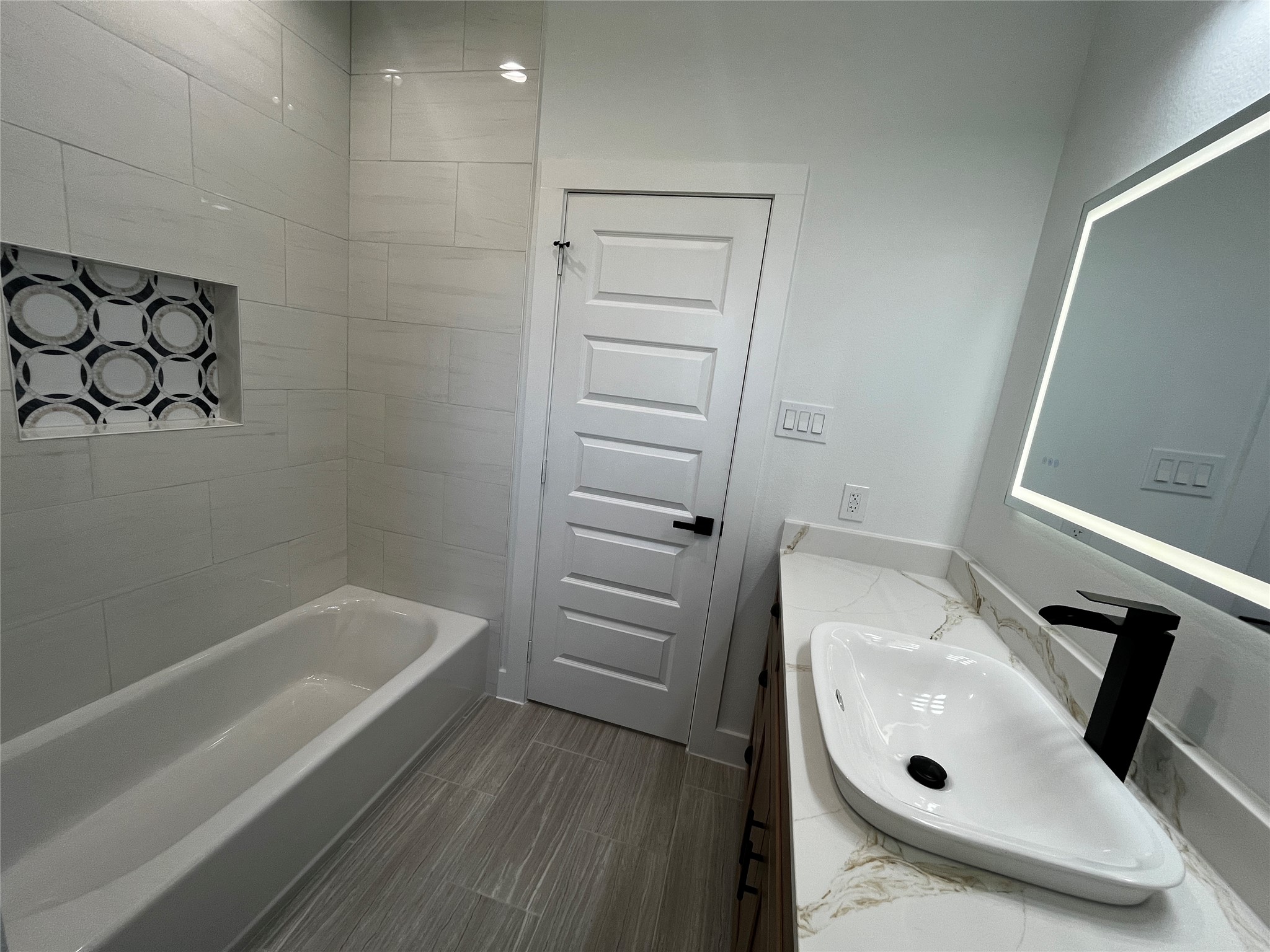 471 Buffalo Trail Angleton, TX 77515 - Photo 22 of 35 Bright and modern bathroom featuring a sleek bathtub with a decorative tile niche, a stylish vanity with a vessel sink, and an illuminated mirror. The space is enhanced by light tile flooring and contemporary fixtures.
