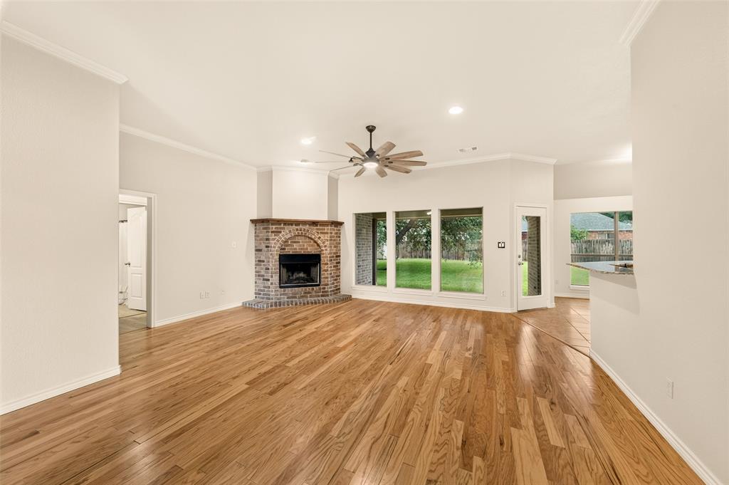 2105 Ridgewood Drive Bridgeport, TX 76426 - Photo 7 of 27 Spacious living area featuring wood-finish flooring, a brick fireplace with an arched opening, multiple large windows, a ceiling fan with integrated lighting, and crown molding