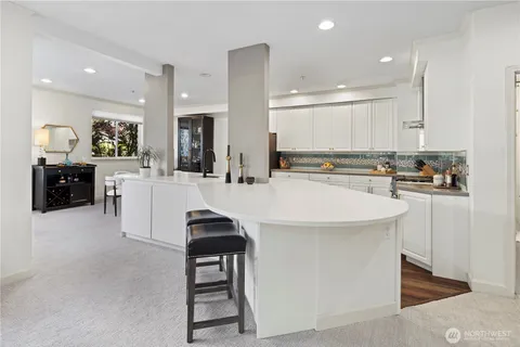 a kitchen with stainless steel appliances kitchen island granite countertop a sink a stove a refrigerator and white cabinets with wooden floor