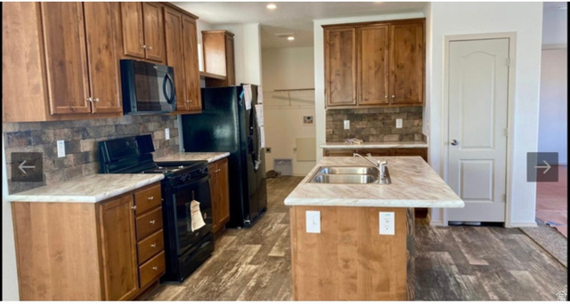 289 West Center Street Hinckley, UT 84635 - Photo 2 of 13 Kitchen featuring wood-finish cabinetry, black appliances, a central island with an undermount sink, and wood-finish flooring