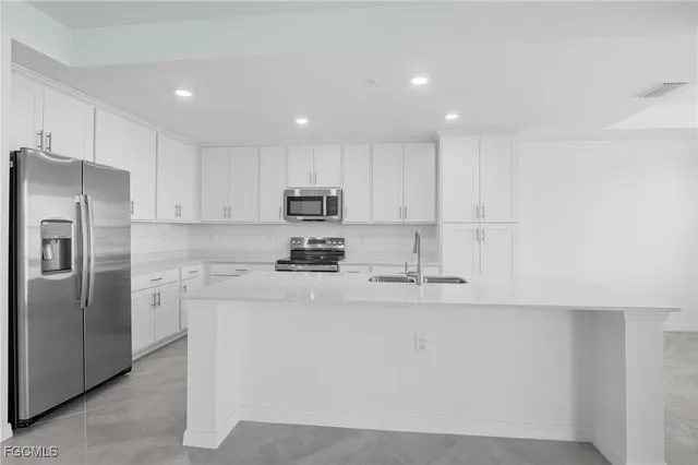 a kitchen with stainless steel appliances granite countertop white cabinets a sink a stove a refrigerator and white cabinets