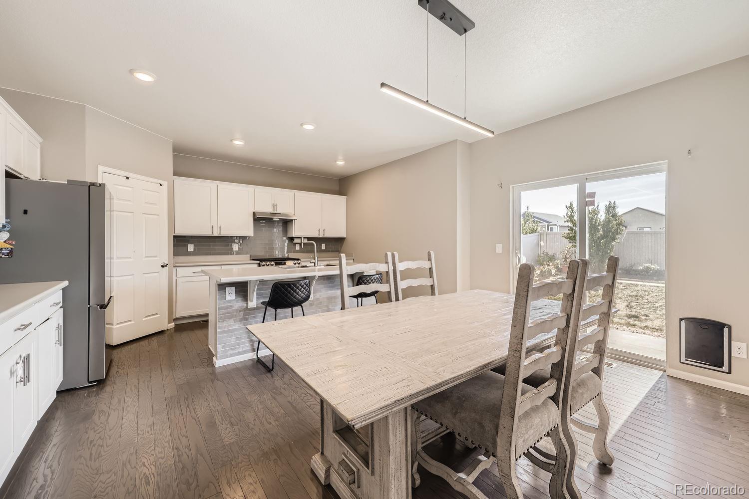 6808 Morrison Drive Frederick, CO 80530 - Photo 9 of 28 a kitchen with stainless steel appliances granite countertop a stove a refrigerator a microwave oven a dining table and chairs with wooden floor