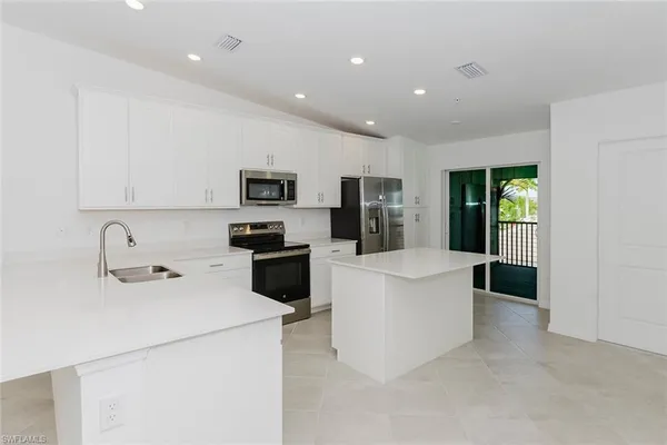 a kitchen with stainless steel appliances a stove a sink a microwave a refrigerator a white cabinets and couches