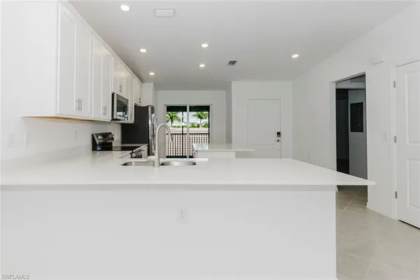 a large white kitchen with stainless steel appliances a sink a stove a microwave a refrigerator and white cabinets