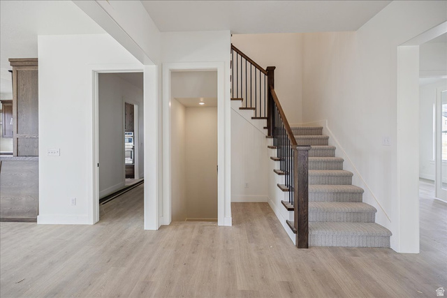 7189 South Sage Road, Unit 214 West Jordan, UT 84081 - Photo 12 of 29 Foyer featuring light wood-finish flooring, a carpeted staircase with dark wood newel posts, and metal balusters