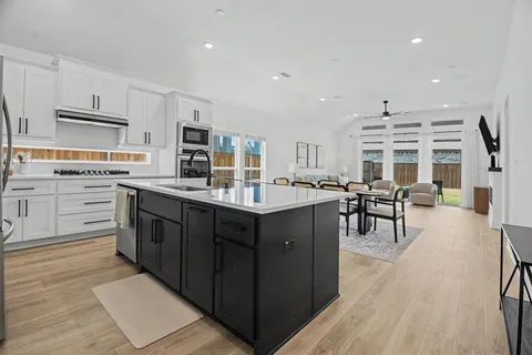 a kitchen with stainless steel appliances kitchen island granite countertop a stove top oven a sink dishwasher a dining table and chairs with wooden floor