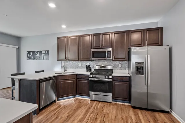 a kitchen with stainless steel appliances granite countertop a stove a sink dishwasher a refrigerator and a microwave oven with wooden floor