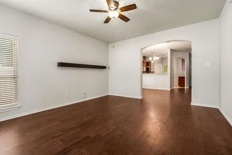 an empty room with wooden floor chandelier fan and windows